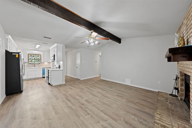 unfurnished living room with ceiling fan, light hardwood / wood-style floors, a textured ceiling, and a brick fireplace