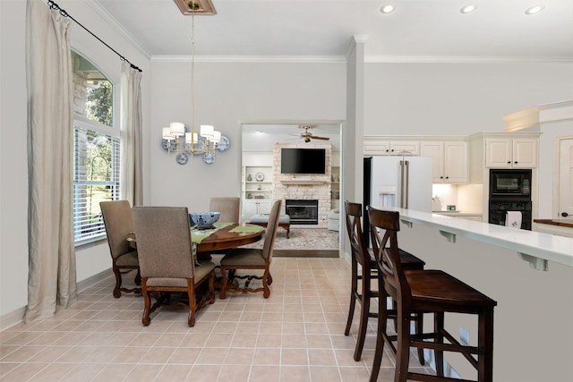 dining space with light tile patterned flooring, a fireplace, crown molding, and ceiling fan with notable chandelier