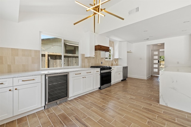 kitchen with beverage cooler, appliances with stainless steel finishes, lofted ceiling, white cabinets, and light hardwood / wood-style floors