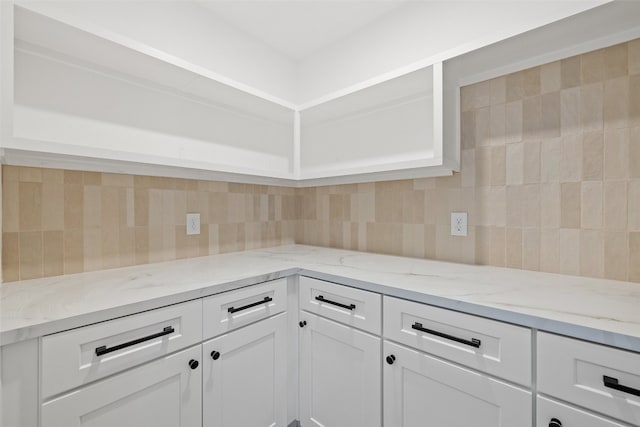 kitchen featuring white cabinets, light stone countertops, and backsplash