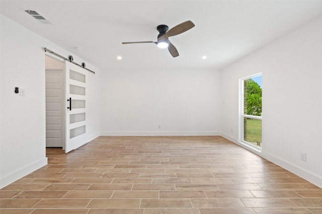 unfurnished room with light hardwood / wood-style flooring, ceiling fan, and a barn door