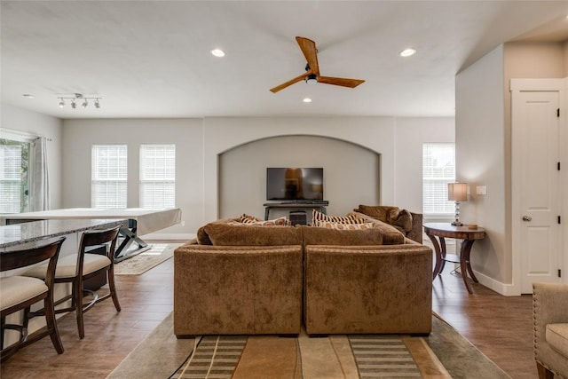 living room with a wealth of natural light, ceiling fan, and dark wood-type flooring