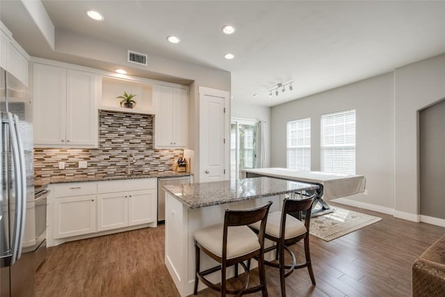 kitchen with sink, stone counters, appliances with stainless steel finishes, white cabinets, and a kitchen island