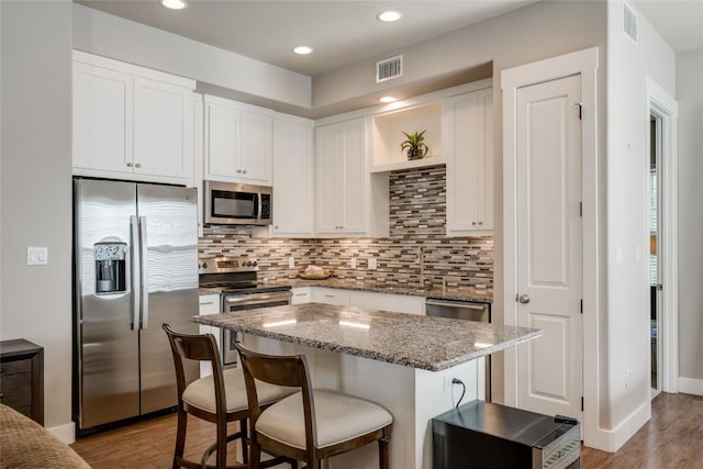 kitchen with white cabinetry, light stone countertops, stainless steel appliances, light hardwood / wood-style flooring, and a breakfast bar