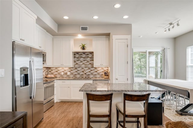 kitchen featuring track lighting, light stone counters, stainless steel appliances, white cabinets, and a kitchen island