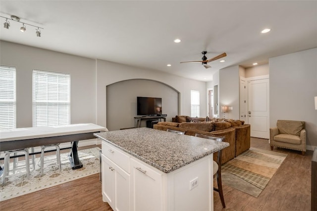 kitchen featuring a kitchen island, a breakfast bar, white cabinets, light stone countertops, and dark wood-type flooring