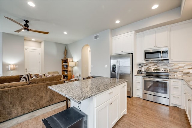 kitchen with a center island, stainless steel appliances, a kitchen bar, decorative backsplash, and white cabinets