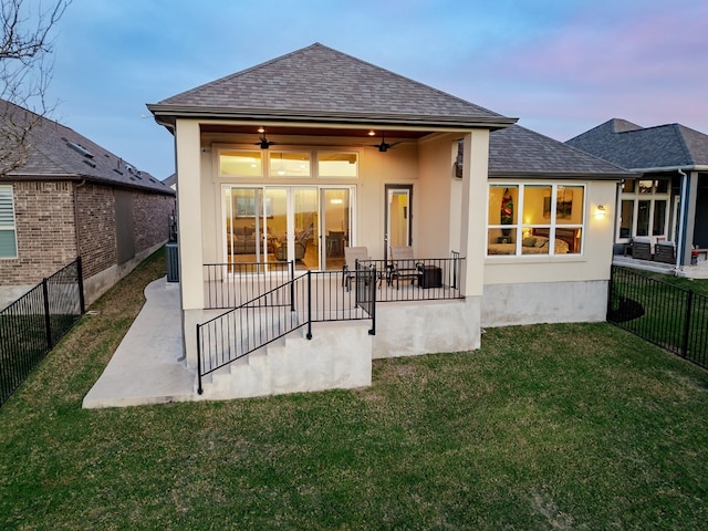 back house at dusk featuring a patio, central AC, ceiling fan, and a yard