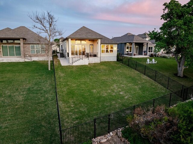 back house at dusk featuring a patio and a yard