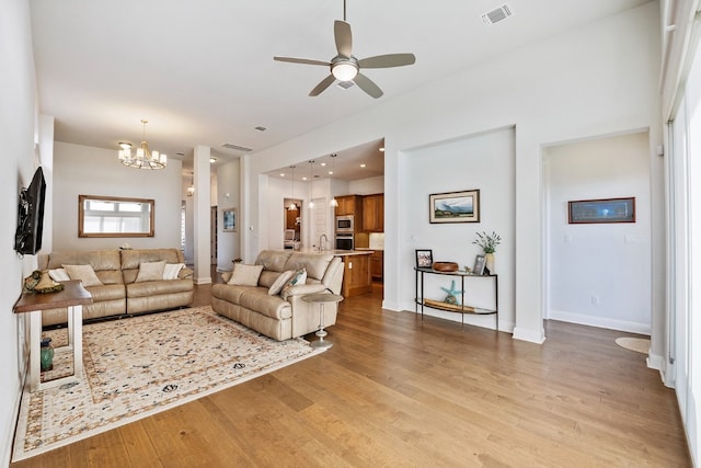 living room with ceiling fan with notable chandelier and light hardwood / wood-style floors