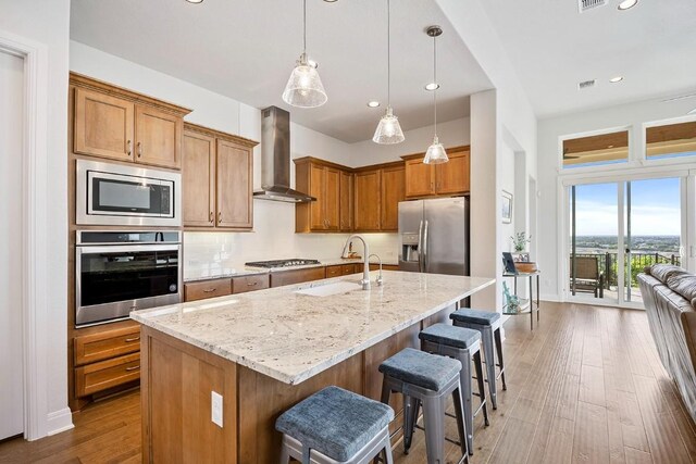 kitchen with dark hardwood / wood-style flooring, stainless steel appliances, a kitchen island with sink, sink, and wall chimney range hood