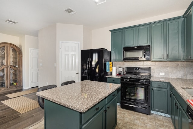 kitchen featuring light stone counters, a kitchen island, black appliances, green cabinetry, and tasteful backsplash