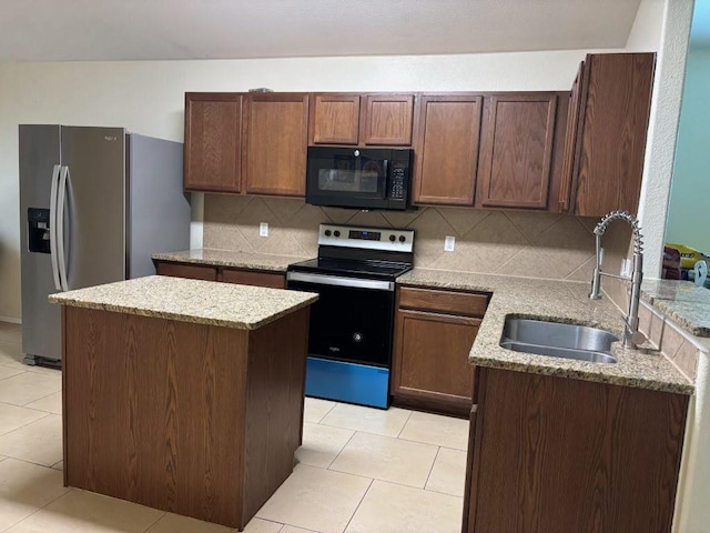 kitchen featuring appliances with stainless steel finishes, a sink, backsplash, light stone counters, and a center island
