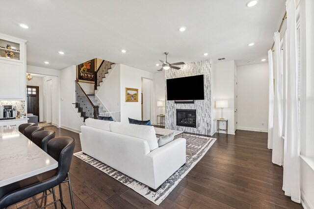 living room featuring dark wood-type flooring, recessed lighting, a large fireplace, and stairway