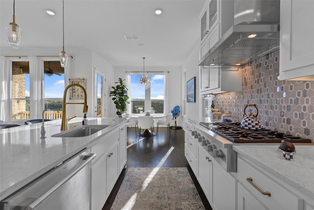 kitchen featuring stainless steel appliances, decorative backsplash, white cabinetry, a sink, and wall chimney range hood