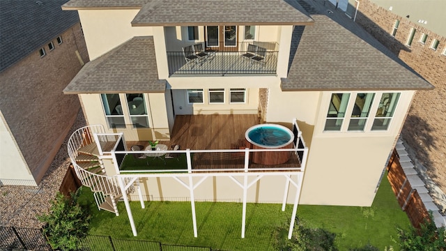 rear view of house with a shingled roof, fence, a balcony, and stucco siding