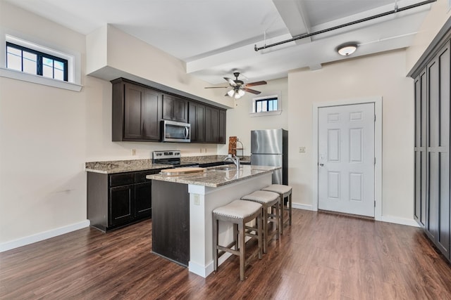 kitchen featuring a kitchen bar, stainless steel appliances, dark wood-type flooring, and light stone countertops