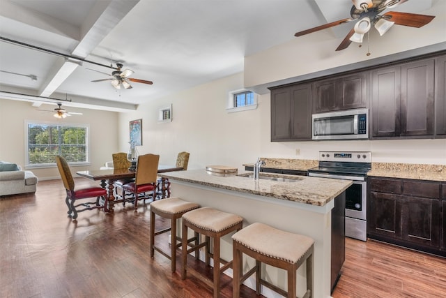 kitchen featuring dark brown cabinetry, an island with sink, sink, appliances with stainless steel finishes, and light wood-type flooring