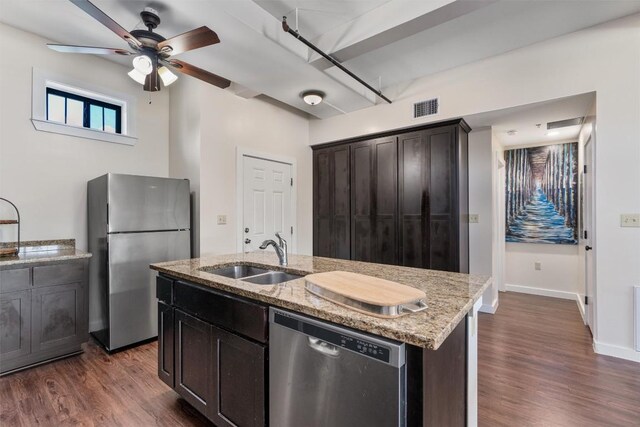 kitchen featuring an island with sink, sink, dark wood-type flooring, stainless steel appliances, and light stone countertops