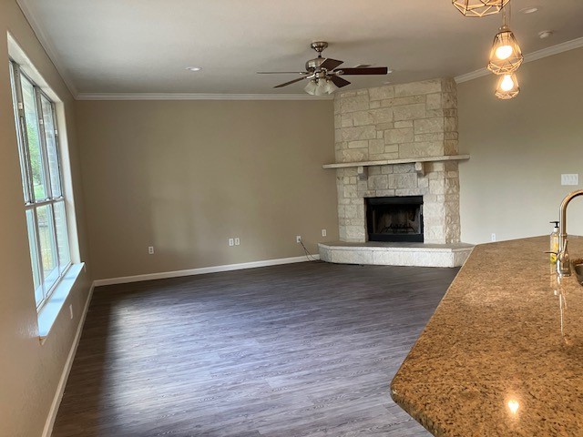 unfurnished living room featuring ceiling fan, dark hardwood / wood-style floors, crown molding, and a stone fireplace