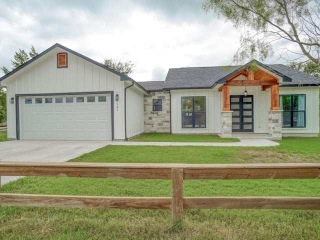 modern inspired farmhouse with a garage, a shingled roof, driveway, stone siding, and a front yard