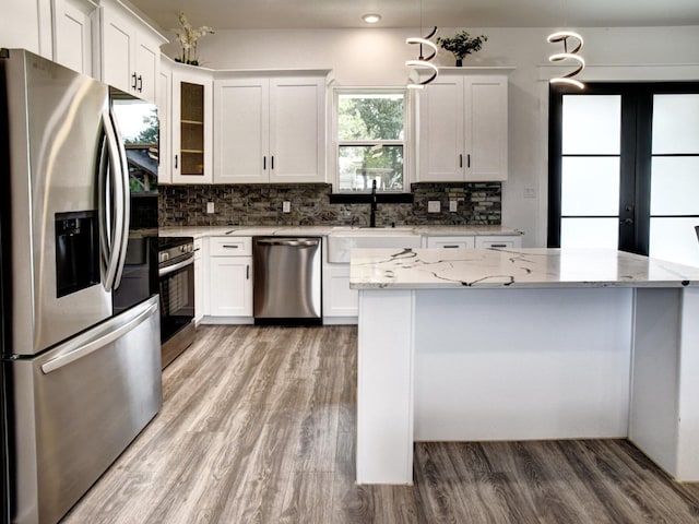 kitchen with pendant lighting, white cabinets, light hardwood / wood-style floors, and stainless steel appliances