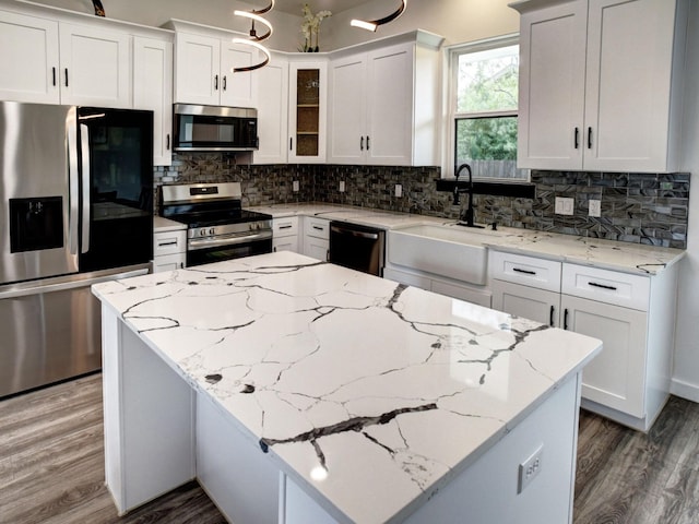 kitchen with a sink, wood finished floors, appliances with stainless steel finishes, backsplash, and a center island