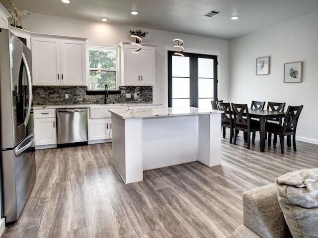 kitchen featuring stainless steel appliances, wood-type flooring, white cabinets, a kitchen island, and pendant lighting