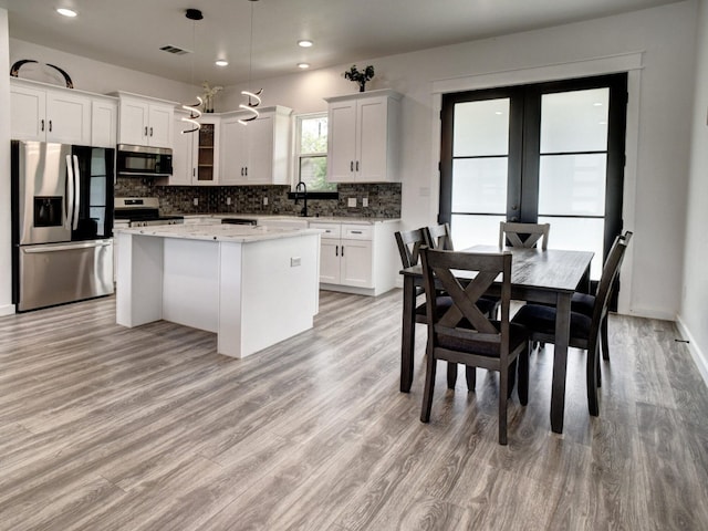 kitchen featuring stainless steel appliances, light hardwood / wood-style floors, white cabinetry, hanging light fixtures, and a kitchen island