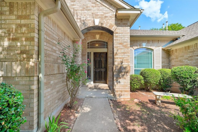 property entrance featuring brick siding and a shingled roof