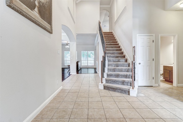 stairs with a high ceiling, ceiling fan, and tile patterned floors