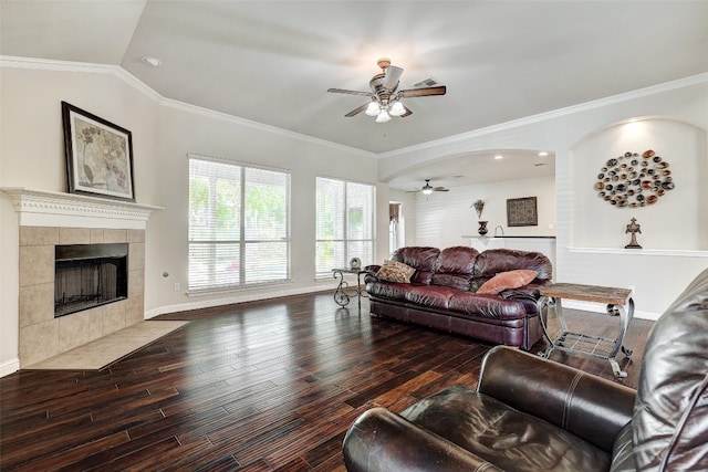 living room featuring vaulted ceiling, dark hardwood / wood-style floors, a tiled fireplace, ornamental molding, and ceiling fan