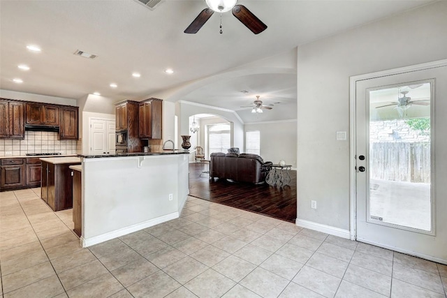 kitchen with light tile patterned floors, visible vents, arched walkways, decorative backsplash, and under cabinet range hood