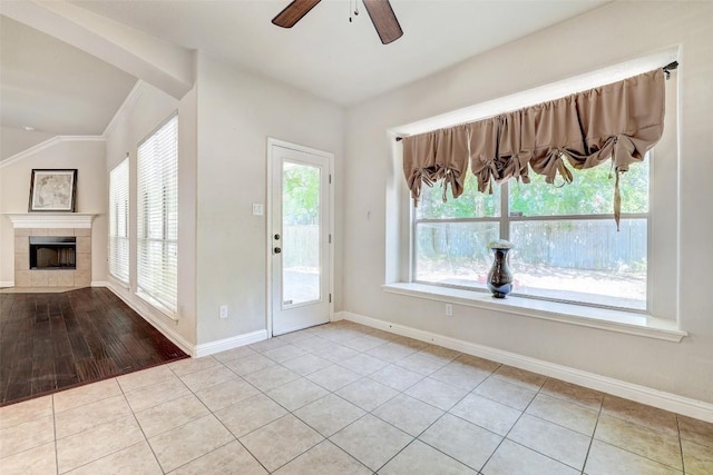 tiled foyer with a ceiling fan, baseboards, a fireplace, vaulted ceiling, and crown molding