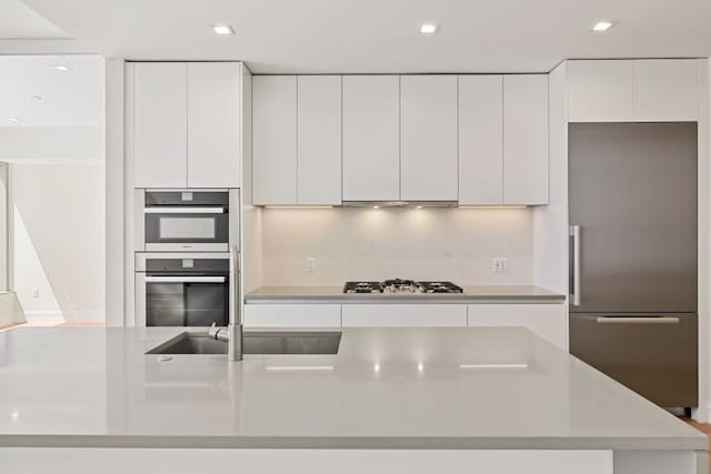 kitchen featuring tasteful backsplash, white cabinets, range hood, and appliances with stainless steel finishes