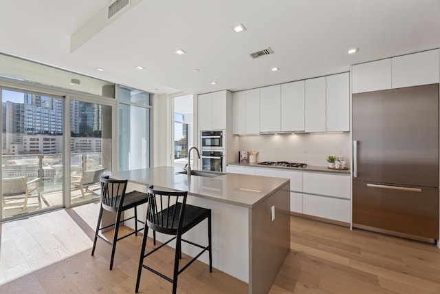 kitchen with a kitchen island with sink, white cabinets, light hardwood / wood-style floors, and appliances with stainless steel finishes