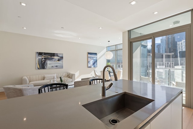 kitchen featuring white cabinetry, sink, hanging light fixtures, and light wood-type flooring