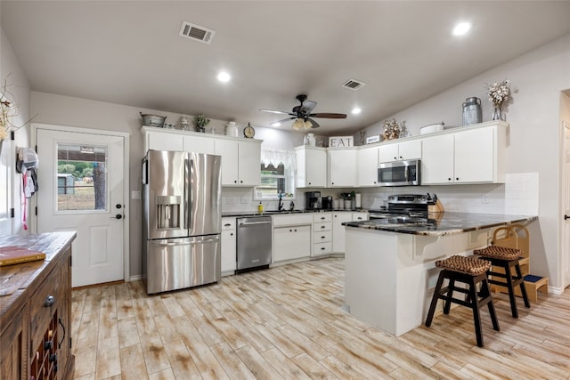 kitchen with light hardwood / wood-style flooring, backsplash, kitchen peninsula, ceiling fan, and appliances with stainless steel finishes