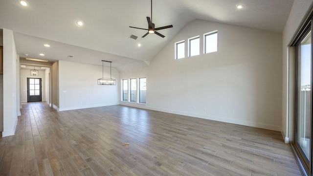 unfurnished living room featuring ceiling fan with notable chandelier, high vaulted ceiling, baseboards, and light wood-style floors