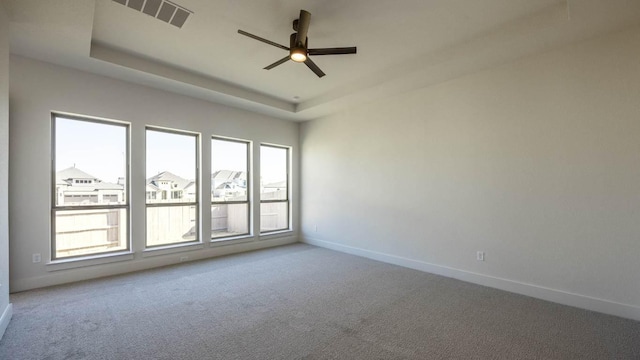 carpeted empty room featuring visible vents, a tray ceiling, a ceiling fan, and baseboards