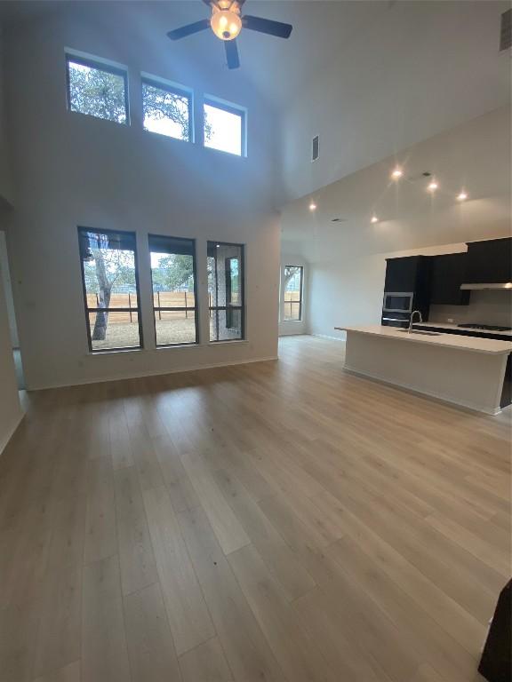 unfurnished living room with ceiling fan, a towering ceiling, sink, and light hardwood / wood-style flooring