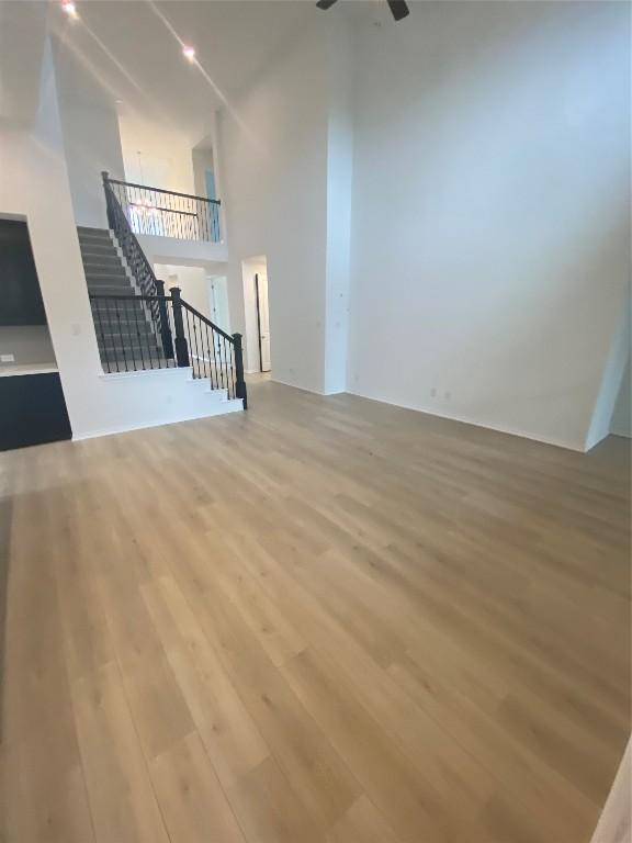 unfurnished living room featuring a high ceiling, ceiling fan, and light hardwood / wood-style flooring