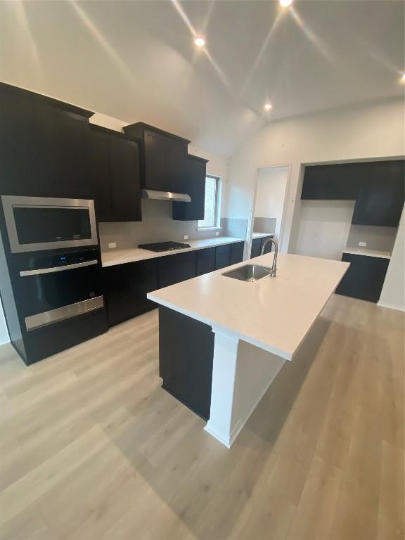 kitchen featuring sink, black gas stovetop, light hardwood / wood-style floors, and a center island with sink