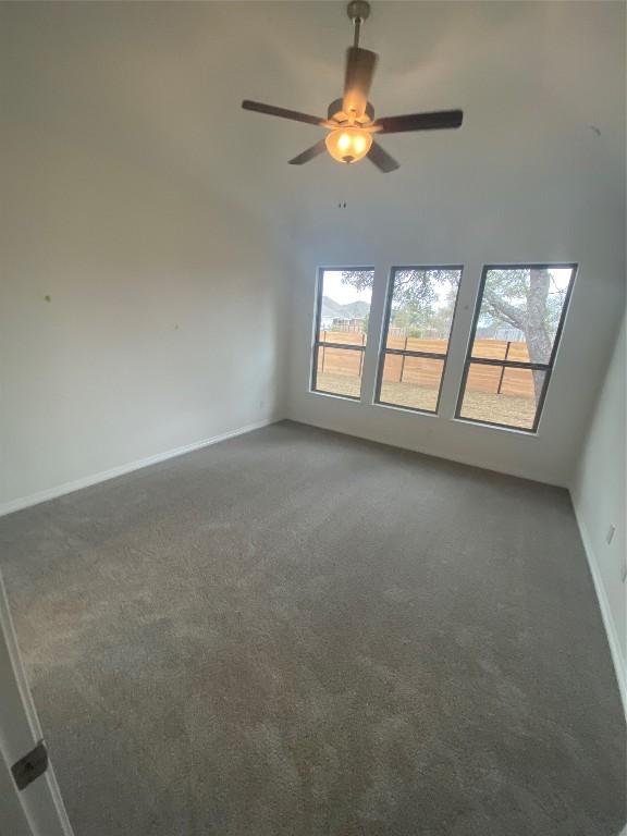 unfurnished room with ceiling fan, plenty of natural light, and dark colored carpet