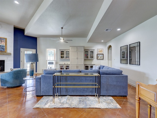 living room featuring tile patterned flooring, ceiling fan, a fireplace, and a textured ceiling