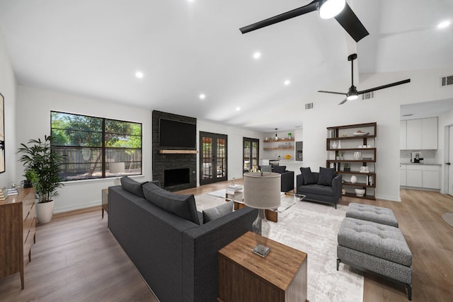 living room featuring a fireplace, high vaulted ceiling, ceiling fan, and light hardwood / wood-style floors