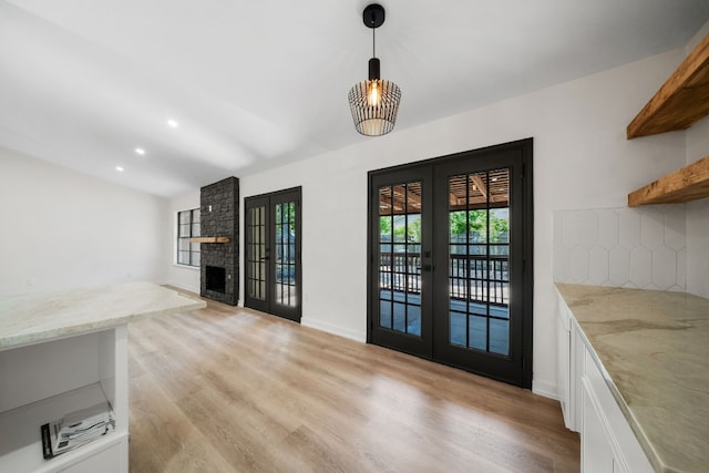 doorway with an inviting chandelier, a fireplace, french doors, lofted ceiling, and light wood-type flooring