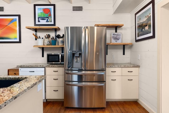 kitchen featuring light stone countertops, dark wood-type flooring, stainless steel appliances, wood walls, and white cabinets