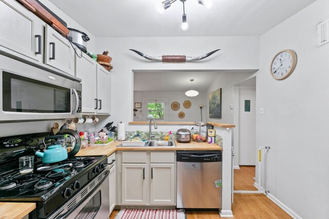 kitchen with light wood finished floors, appliances with stainless steel finishes, a sink, and butcher block counters