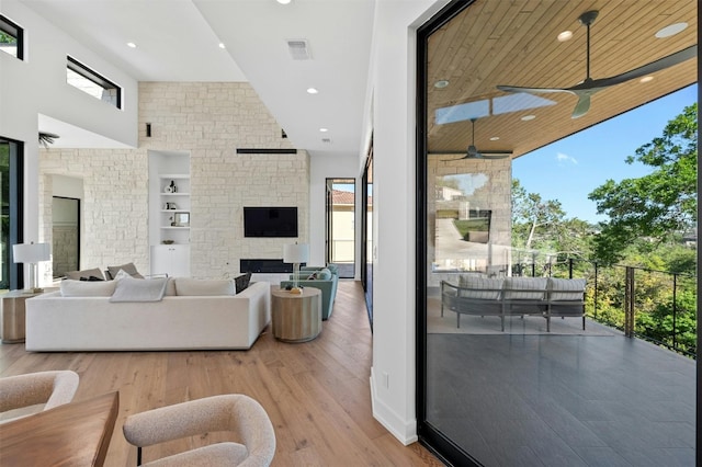 living room featuring built in shelves, a towering ceiling, light hardwood / wood-style flooring, and a wealth of natural light